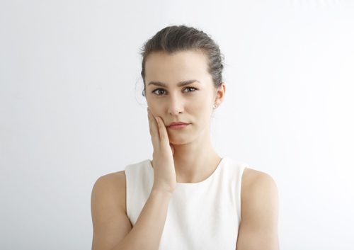 Frowning woman touching cheek due to tooth pain